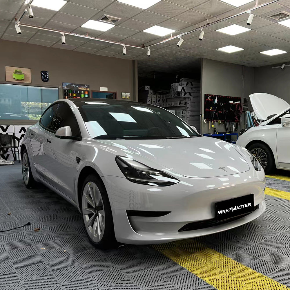 Tesla Model 3 wrapped in Nardo Gray super gloss vinyl inside a wrap shop, front three quarter view